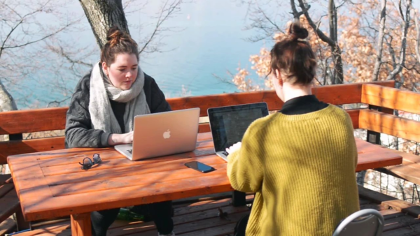 Twee studenten buiten aan het werk met laptop aan picknicktafel, uitzicht over Meer van Ohrid