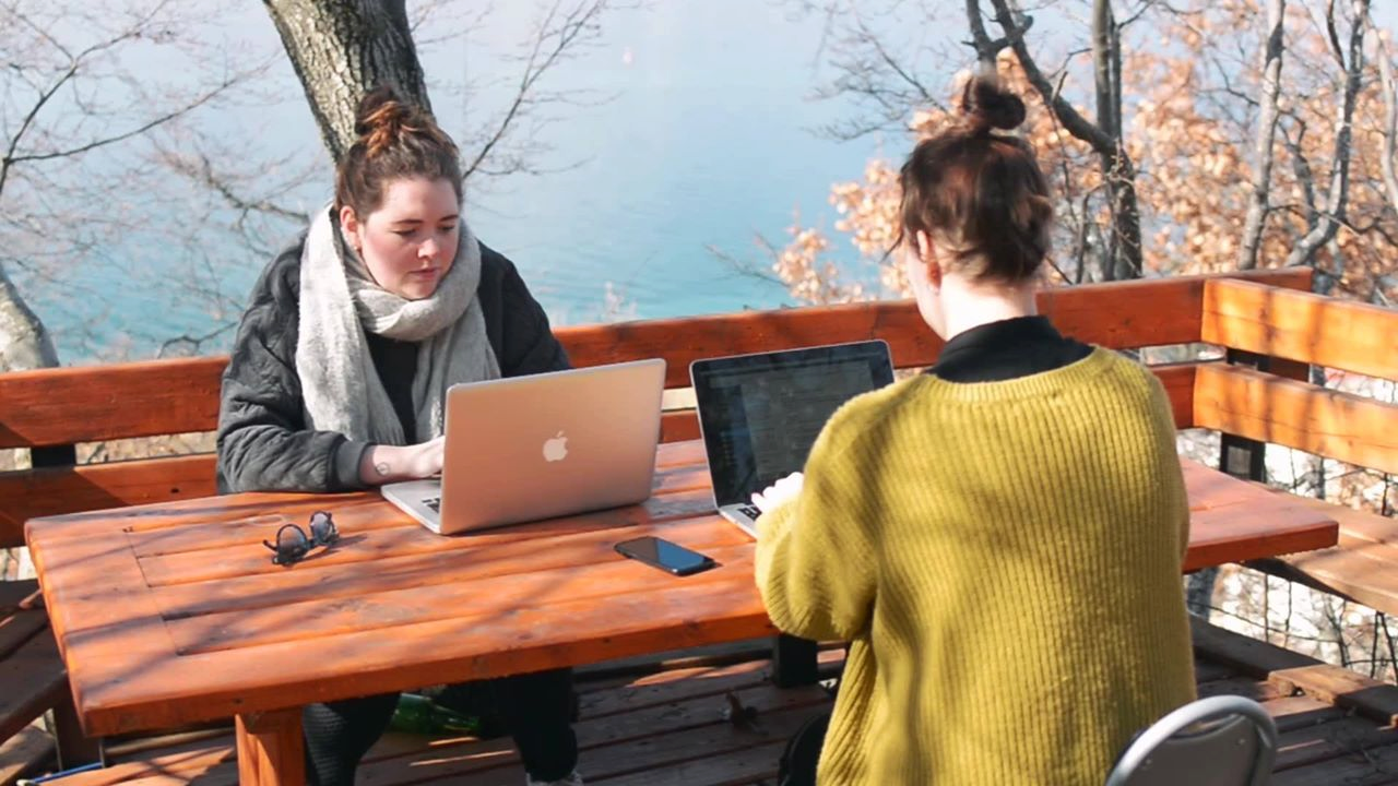 Twee studenten buiten aan het werk met laptop aan picknicktafel, uitzicht over Meer van Ohrid